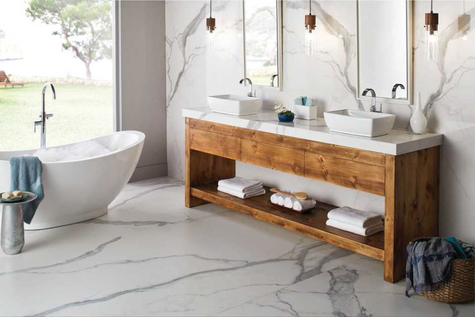 marble tile floor in bathroom with marble walls, wood vanity and deep soak tub